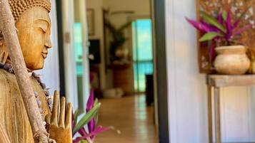 A statue with a serene expression, a wooden structure with a textured surface, and a potted plant with broad leaves.