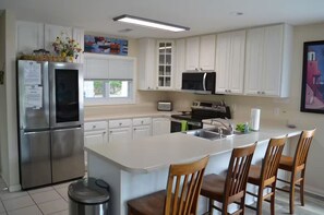 Una cocina moderna con armarios blancos, electrodomésticos de acero inoxidable, una isla grande con taburetes altos y una ventana con persianas.