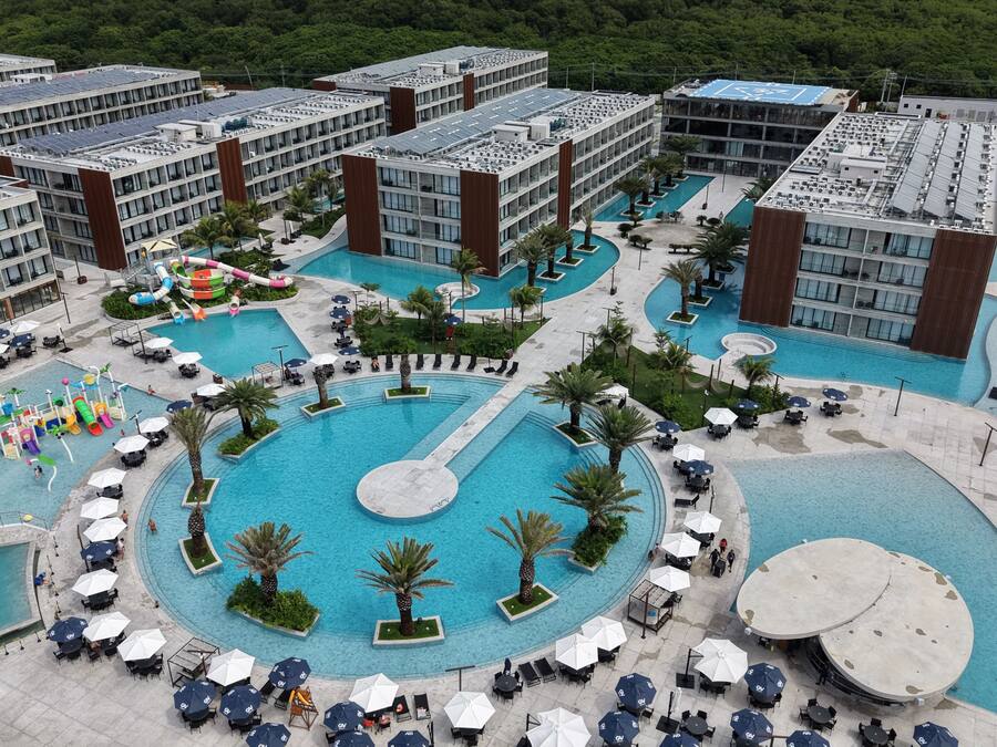 Un hotel con varias piscinas, una zona de juegos para niños y mobiliario de exterior.