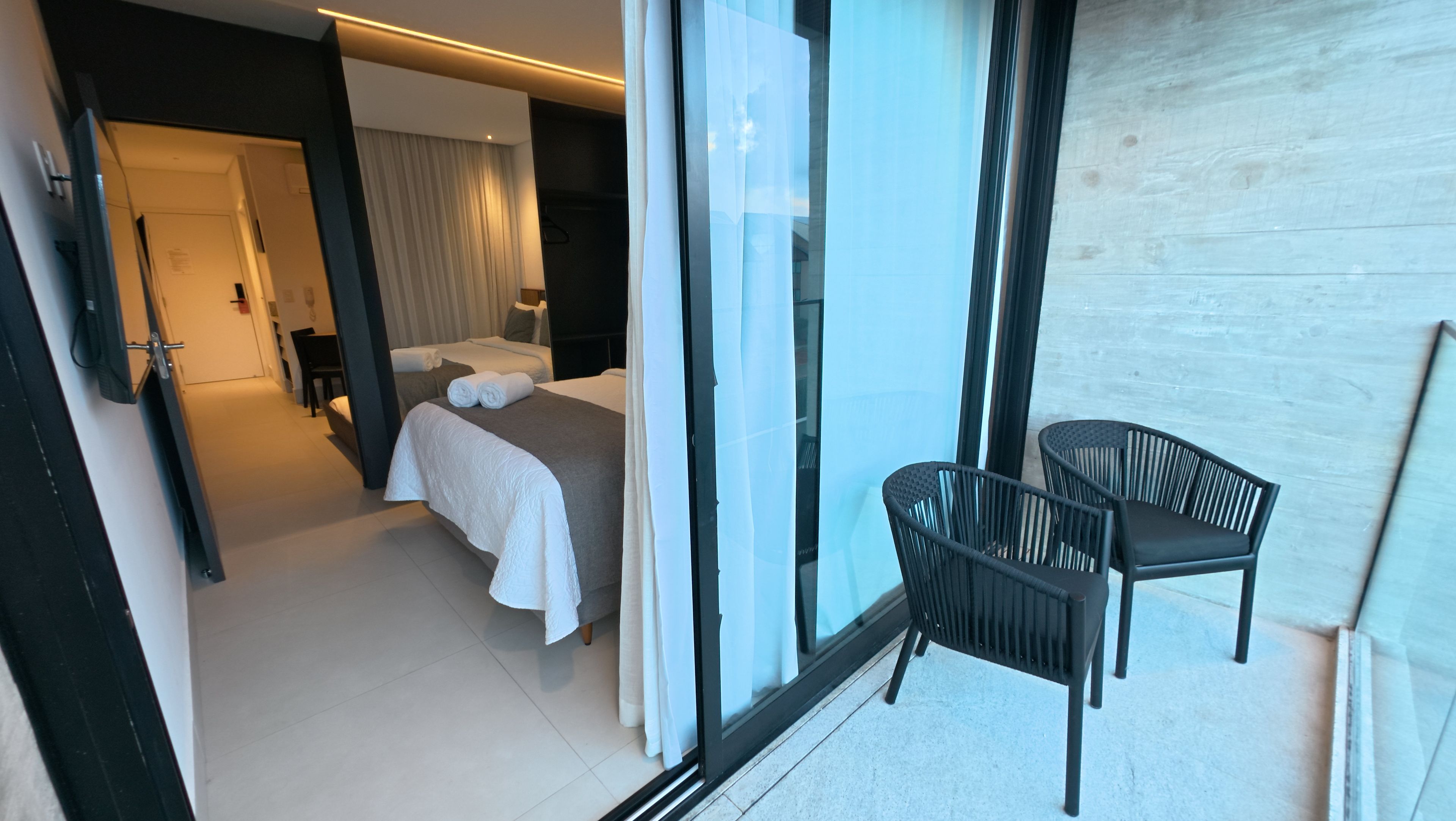 A hotel room with a bed, a small table, two chairs, and a view through a glass door.