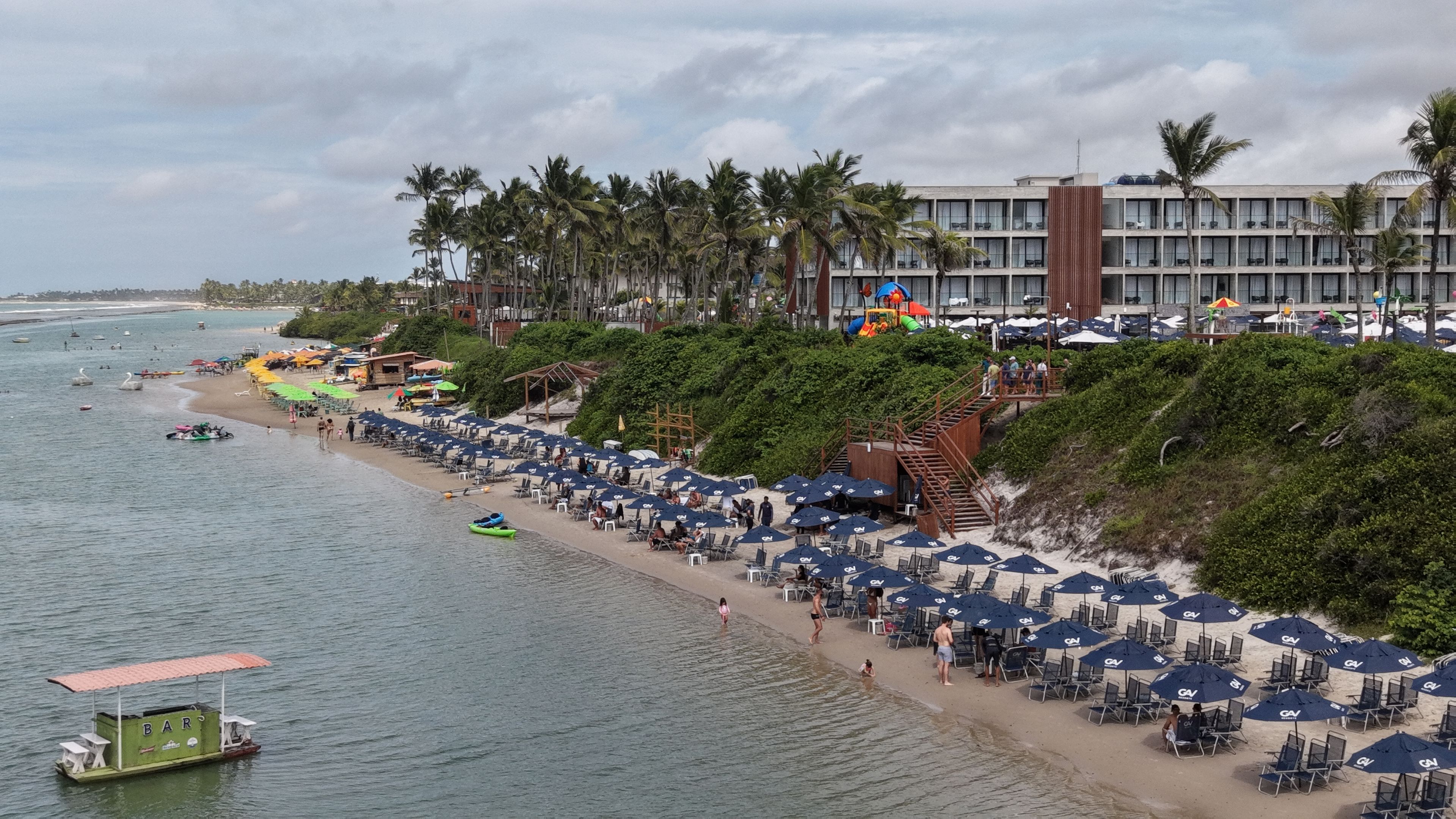 Una playa con hileras de sombrillas y sillas, una torre de salvavidas y un edificio con varios balcones.