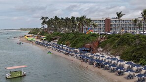 A beach with rows of umbrellas and chairs, a lifeguard tower, and a building with multiple balconies. - Porto 2 Life Resort - GAV Resorts (Ipojuca)