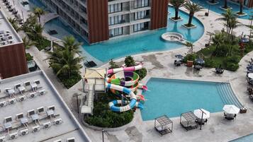 Zona de piscina de hotel con tobogán de agua, sillas de descanso y un edificio con balcones.