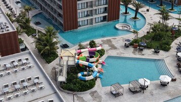 Zona de piscina de hotel con tobogán de agua, sillas de descanso y un edificio con balcones.