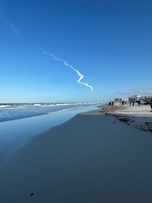 Ein Strand mit blauem Himmel, Wellen und einer Flugzeugspur.