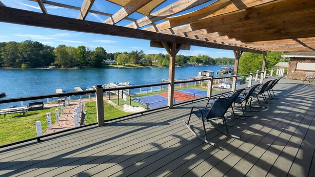 En inglasad veranda med utsikt över en sjö, utomhusmöbler och en tennisbana.