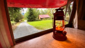 A lantern on a table by a window with a view of a green landscape and a red-roofed building. - "Darla" the Glamping Trailer at Ashford Lodge (Ashford)
