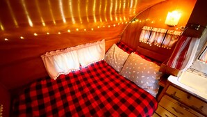 A cozy room with a checkered bedspread, a wooden dresser, and string lights. - "Darla" the Glamping Trailer at Ashford Lodge (Ashford)