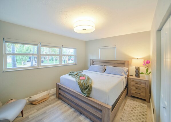 A bedroom with a bed, bedside tables, a lamp, and a window with a view of trees and parked cars. - Tropical Pool Oasis. Near beach, Wilton Manors and Fort Lauderdale (Fort Lauderdale)