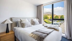 Ein Hotelzimmer mit einem großen Bett, einem Nachttisch, einer Lampe und Blick auf eine Landschaft durch ein Fenster.