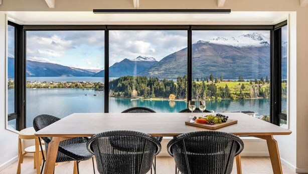 Een eetruimte met een tafel en stoelen, met uitzicht op een meer, bergen en een golfbaan.