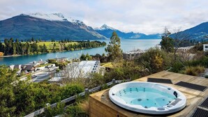 Een hottub op een houten terras met uitzicht op een meer en bergen.