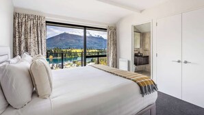 Een slaapkamer met een groot bed, uitzicht op bergen en een meer, een badkamer met een spiegel, en een kledingkast.