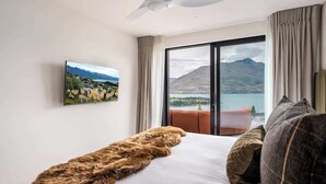 Une chambre d’hôtel avec un lit, une grande fenêtre donnant sur les montagnes, un ventilateur de plafond et un tableau accroché au mur.