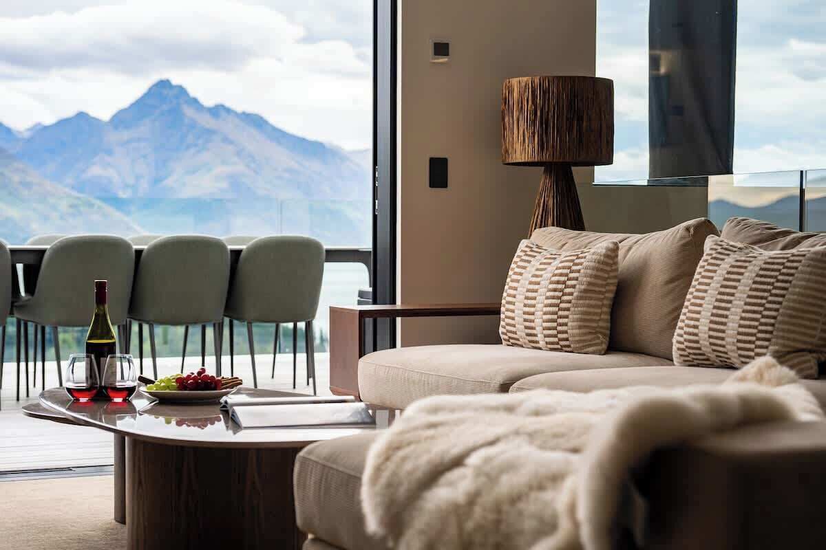 Un salon moderne avec un canapé, des fauteuils, une table sur laquelle se trouvent une bouteille et des verres, et une vue sur les montagnes.