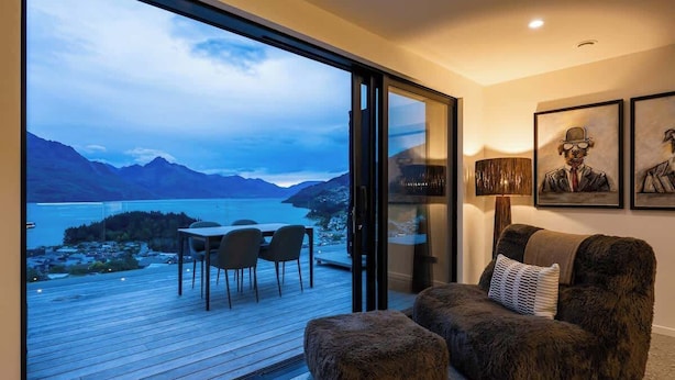 Uma sala de estar moderna com uma grande porta de vidro deslizante que dá para um deck com vista para um lago e montanhas.