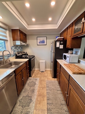 A modern kitchen with stainless steel appliances, wooden cabinets, a patterned rug, and a framed picture on the wall.
