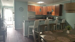 Une cuisine moderne avec des meubles en bois, un réfrigérateur en acier inoxydable et un coin repas avec une table dressée pour six personnes.