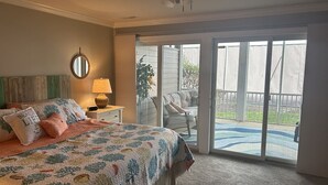 Une chambre à coucher comprenant un lit, un ventilateur de plafond, une fenêtre et une porte-fenêtre coulissante donnant sur un patio.