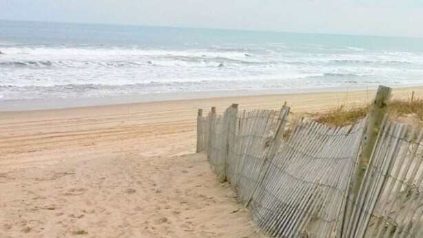 Une plage avec une clôture en bois qui mène à l’eau, une plage de sable et des vagues de l’océan.