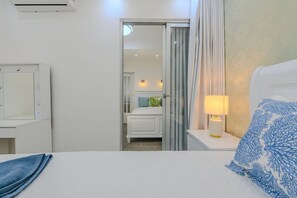 A hotel room with a bed, a nightstand with a lamp, a mirror, and a sliding door leading to a bathroom. - Oasis de Comfort a Pasos del Mar (Boca Chica)
