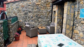 A stone-walled patio with wicker furniture, a table, and potted plants.