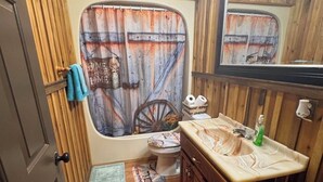 Et rustikt badeværelse med en trækommode, toilet og bruseforhæng med et vintage design.