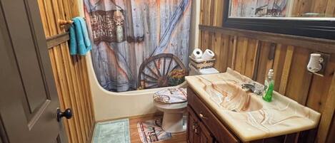 Et rustikt badeværelse med en trækommode, toilet og bruseforhæng med et vintage design.