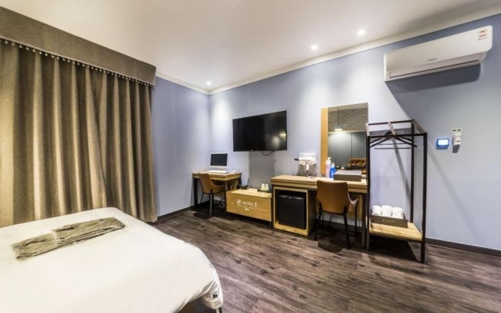 A hotel room with a bed, desk, chair, TV, and a wardrobe.