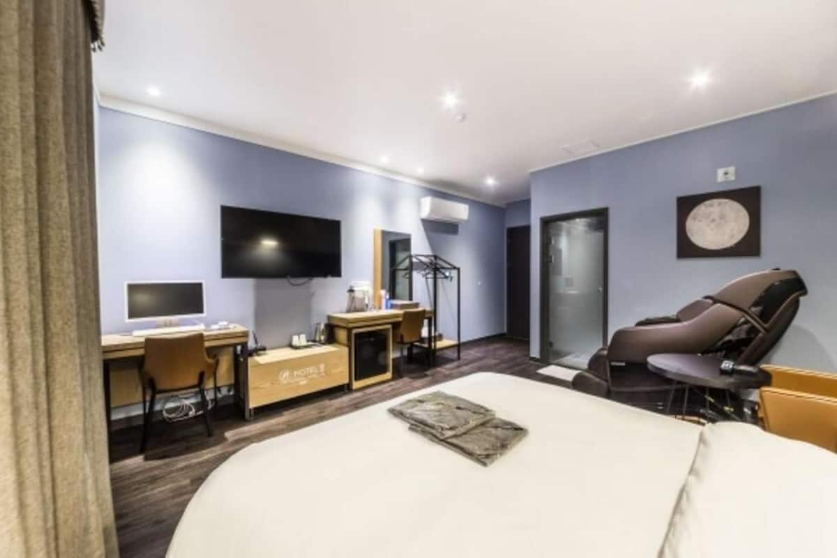 Una habitación de hotel con cama, escritorio, silla, televisor y sillón de masaje.