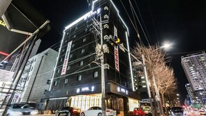 A multi-story hotel with illuminated signage, a visible entrance, and parked cars. - Wol Hotel Seoul (Seoul)