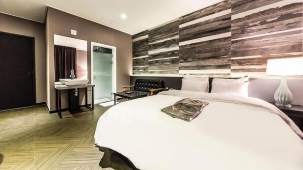 A hotel room with a large bed, a vanity with a mirror, a seating area, and a wall with a wood-like texture. - Wol Hotel Seoul (Seoul)
