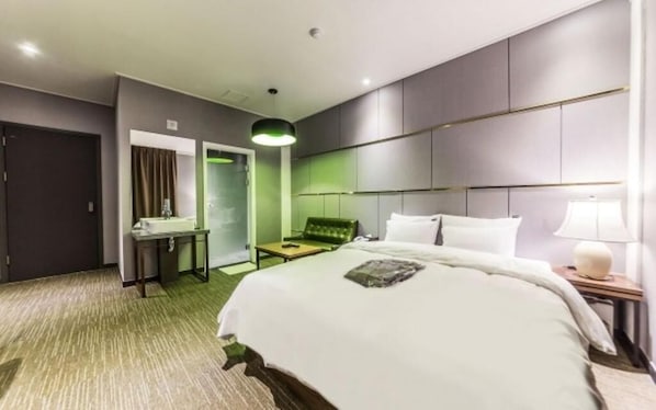 A hotel room with a large bed, a desk, a chair, a bedside table with a lamp, and a green accent wall.