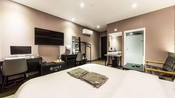 Una habitación de hotel con cama, escritorio, silla, televisor y espejo.