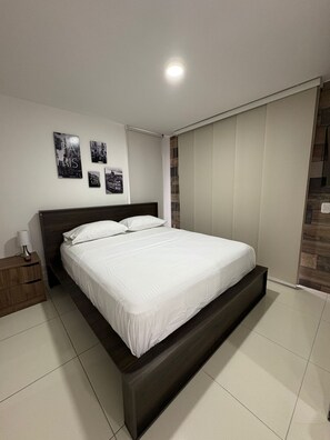 Un dormitorio con una cama grande, una mesita de noche y una lámpara fijada en la pared.