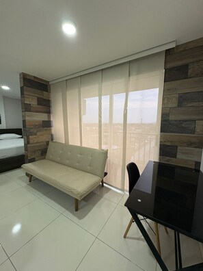 A modern room with a sofa, a dining table, and a view through large windows.