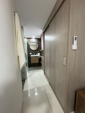 A hallway with a wooden wardrobe, a mirror, a sink, and a towel hanging on the wall.