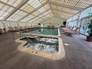 An indoor swimming pool with lounge chairs and a hot tub.