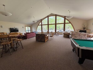 A spacious room with a pool table, comfortable seating, and large windows offering natural light.