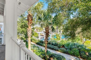 A balcony with a view of a pool area surrounded by lush greenery and palm trees. - Market Street Inn 232/234 - Emerald Escape (Miramar Beach)