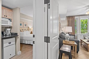 A compact hotel room with a kitchenette, a bed, a seating area, and a view of greenery. - Market Street Inn 232/234 - Emerald Escape (Miramar Beach)