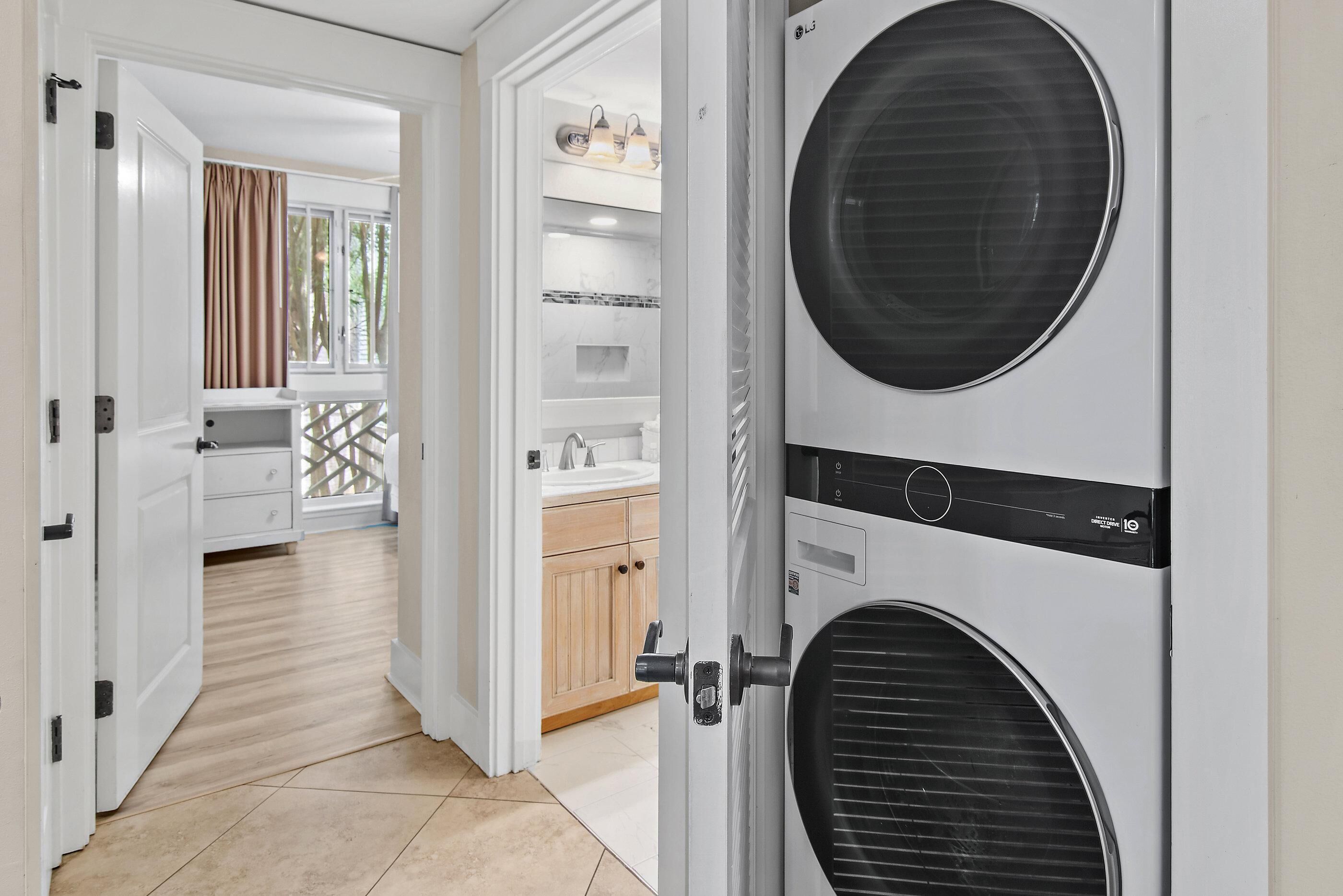 A laundry room with a large wall-mounted dryer, a door leading to a kitchen area, and a view of a balcony with curtains.