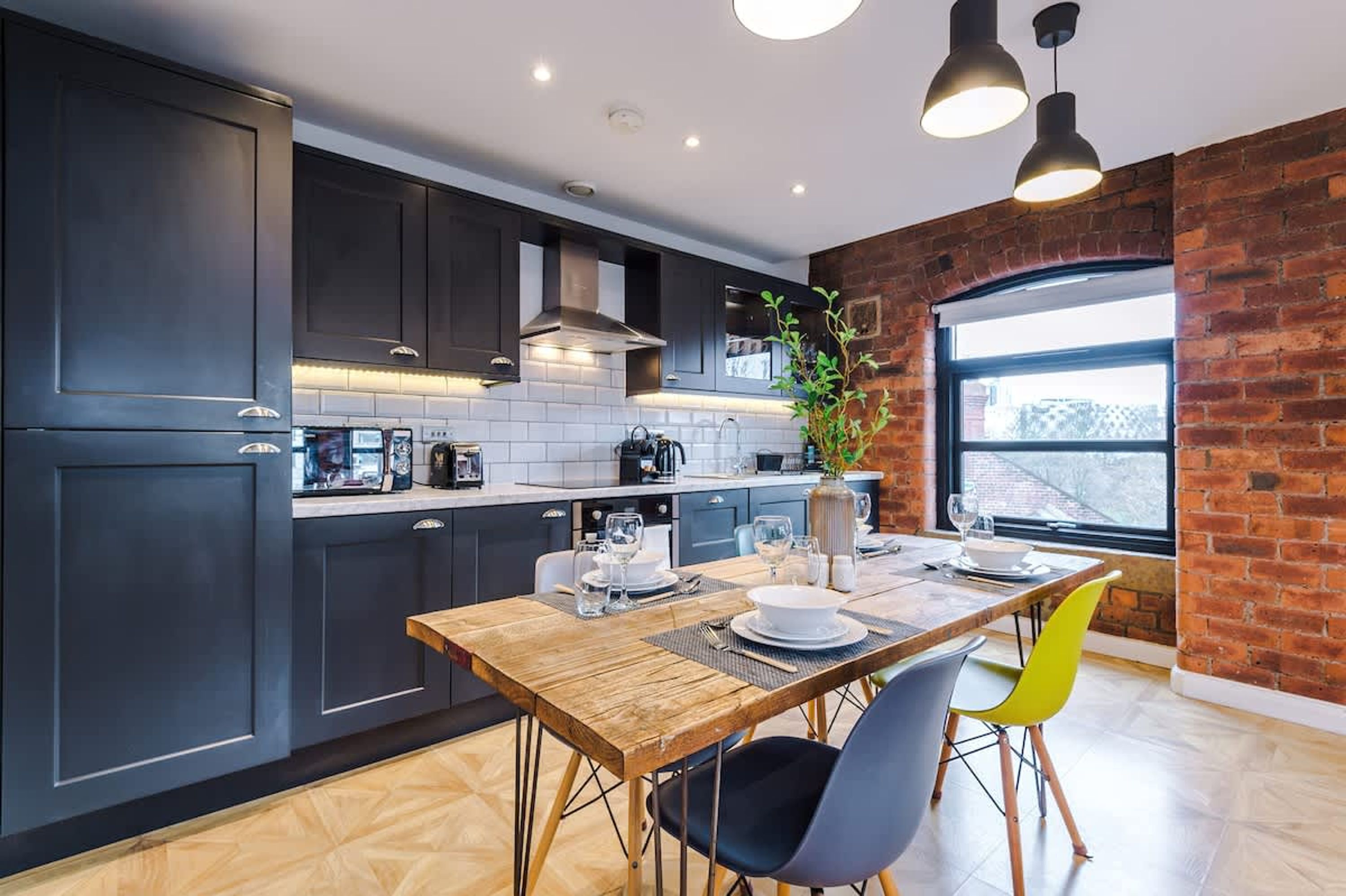 Una cocina moderna con armarios oscuros, una mesa de comedor de madera y una pared de ladrillo.