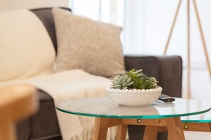 A living room with a glass-top coffee table, a white bowl with a succulent plant, a remote control, and a brown sofa with a beige throw blanket. - Central Harrogate Beautiful Bright 1-bedroom Apartment (Harrogate)