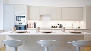 A modern kitchen with white cabinetry, a built-in oven, and a central island with bar stools. - Modern 4-bed Apartment Leeds Business District (Leeds)