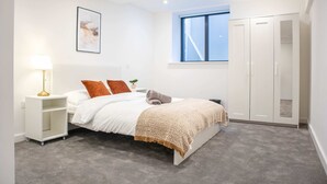 A bedroom with a bed, a bedside lamp, a window, a wardrobe, and a framed picture on the wall. - Modern 4-bed Apartment Leeds Business District (Leeds)