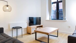 A modern living room with a flat-screen TV, a wooden coffee table, a grey sofa, and a small side table. - Modern 4-bed Apartment Leeds Business District (Leeds)