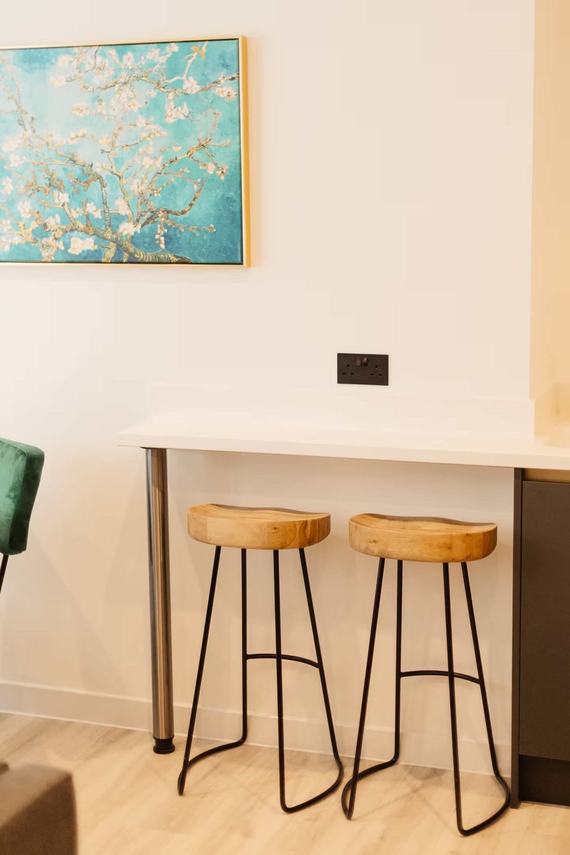 A bar area with a white countertop, two wooden stools with metal legs, and a painting of a tree on the wall.