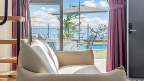Une pièce avec un canapé, donnant sur la piscine, et dotée de parasols à l’extérieur.