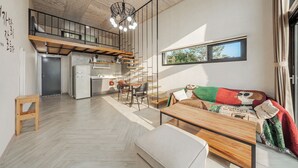 Un appartement moderne de style loft comprenant une cuisine, un coin repas et un espace salon confortable avec un canapé et un pouf.